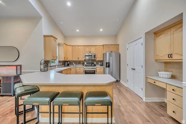 11789 Nicklaus Road Sandy, UT 84092 - Photo 10 of 58 Kitchen with light wood finish cabinets, stainless steel appliances, light countertops, a breakfast bar area, and a peninsula