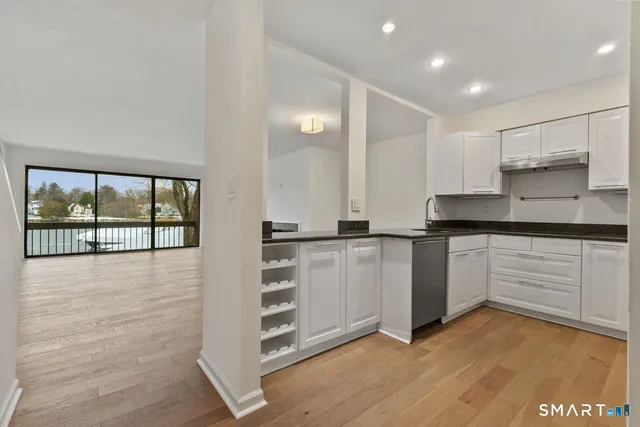 a kitchen with granite countertop a stove a sink and white cabinets with wooden floor
