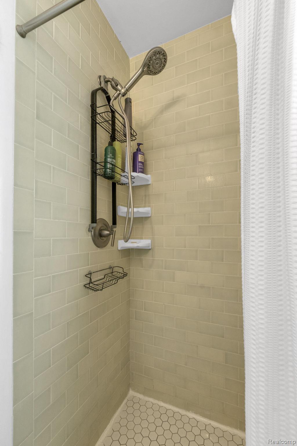 21 Devonshire Road Pleasant Ridge, MI 48069 - Photo 27 of 35 Shower stall featuring subway tile walls, hexagonal floor tiles, a showerhead with an integrated handheld sprayer, and a metal shower caddy