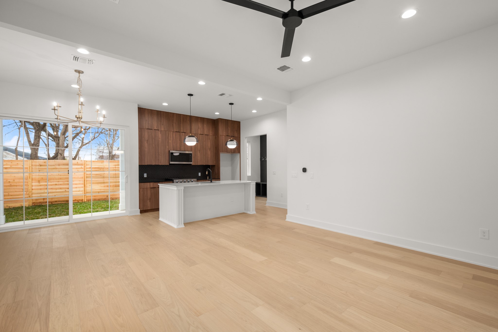 601 Vermont Road, Unit 2 Austin, TX 78702 - Photo 5 of 23 Open-concept living area featuring light wood-finish flooring, a modern kitchen with wood cabinetry and black countertops, a central island, and a sliding glass door opening to a private fenced yard