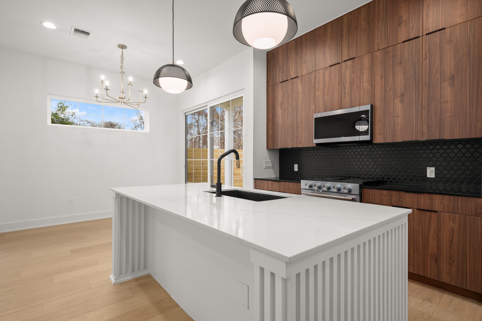 601 Vermont Road, Unit 2 Austin, TX 78702 - Photo 6 of 23 Kitchen featuring a white island with a built-in sink and black faucet, wood-finish cabinetry, stainless steel range, and black tile backsplash