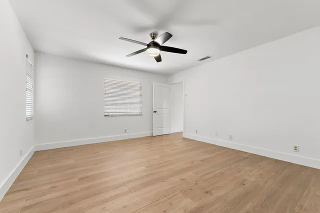 an empty room with wooden floor ceiling fan and windows