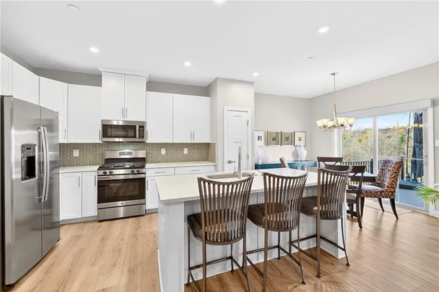 a kitchen with stainless steel appliances kitchen island granite countertop a dining table chairs and a refrigerator