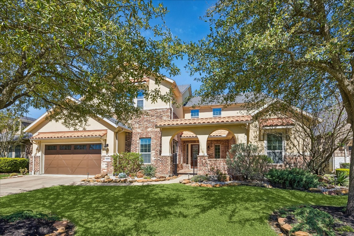 Spanish two-story home with a brick and stucco exterior, arched entry leads to an inviting front courtyard. The well-maintained yard includes lush landscaping and mature trees, providing ample shade and curb appeal. The house also has a spacious three car tandem garage.