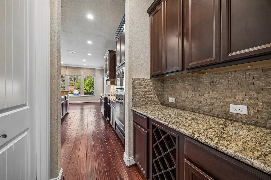 14123 Spindle Arbor Road Cypress, TX 77429 - Photo 11 of 45 Butlers pantry leads from dining area to a modern kitchen with rich wooden cabinetry, granite countertops, and a stylish stone backsplash. The space is well-lit with recessed lighting. Large windows in the breakfast room provide the kitchen with natural light and a view of the backyard.