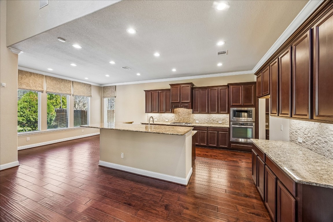 14123 Spindle Arbor Road Cypress, TX 77429 - Photo 12 of 45 Open-concept kitchen and breakfast area with rich hardwood flooring and cabinetry. The kitchen features granite countertops, modern appliances, and ample natural light from large windows with views of well landscaped backyard.