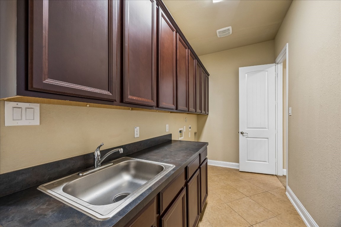 14123 Spindle Arbor Road Cypress, TX 77429 - Photo 24 of 45 Utility room with dark wood cabinets, a stainless steel sink, and ample counter space. The room features neutral walls and tile flooring.