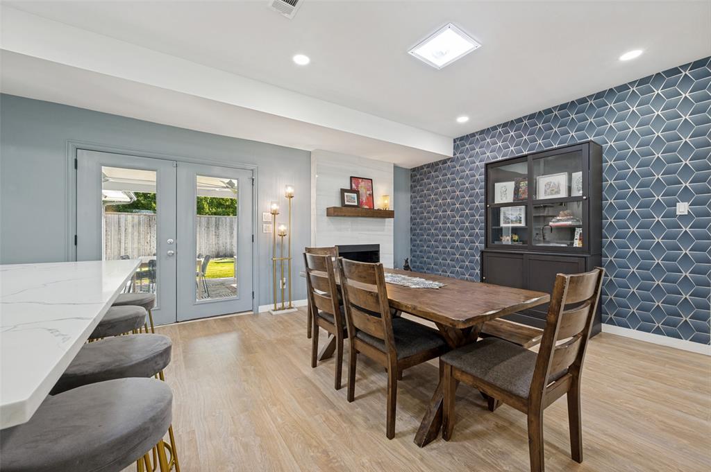 3619 Merrell Road Dallas, TX 75229 - Photo 10 of 26 Dining area featuring a geometric accent wall, wood-finish flooring, and a fireplace with a wood mantle