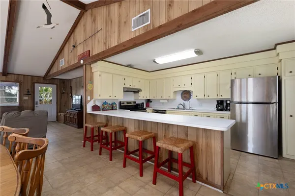 a kitchen with stainless steel appliances a refrigerator a sink dishwasher a dining table and chairs with wooden floor