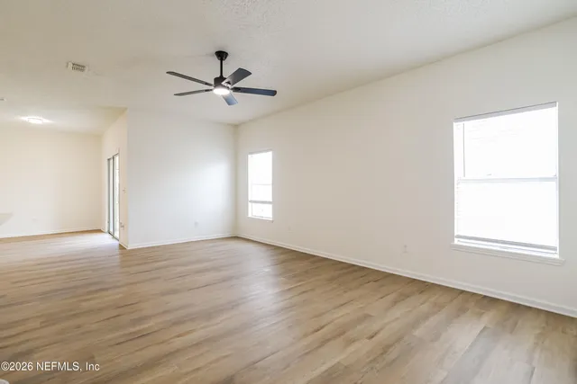 an empty room with wooden floor fan and windows