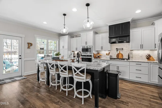 a kitchen with stainless steel appliances granite countertop a stove top oven a refrigerator a sink and a dining table with wooden floor