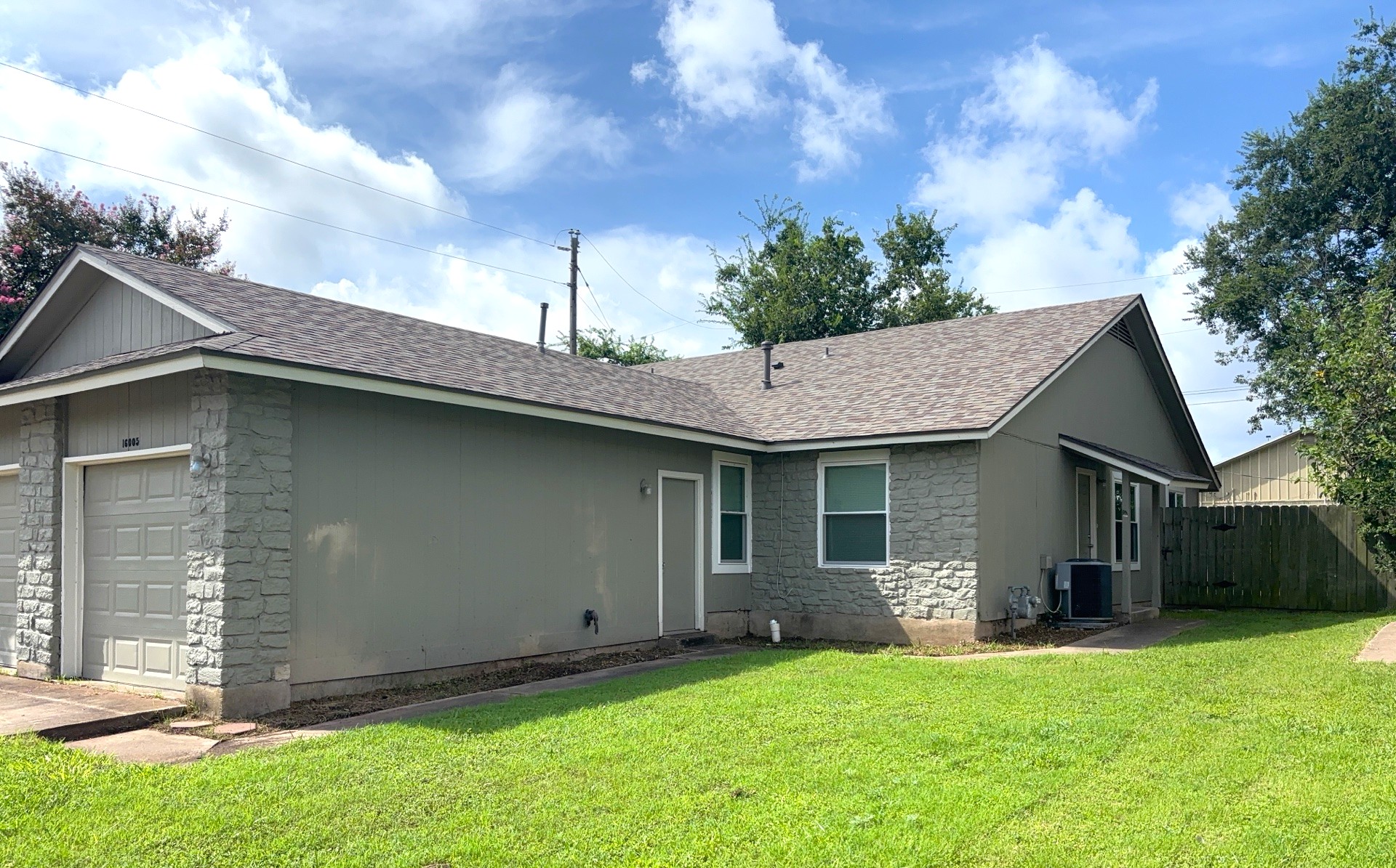 Rear view of house with stone siding, roof with shingles, and a garage