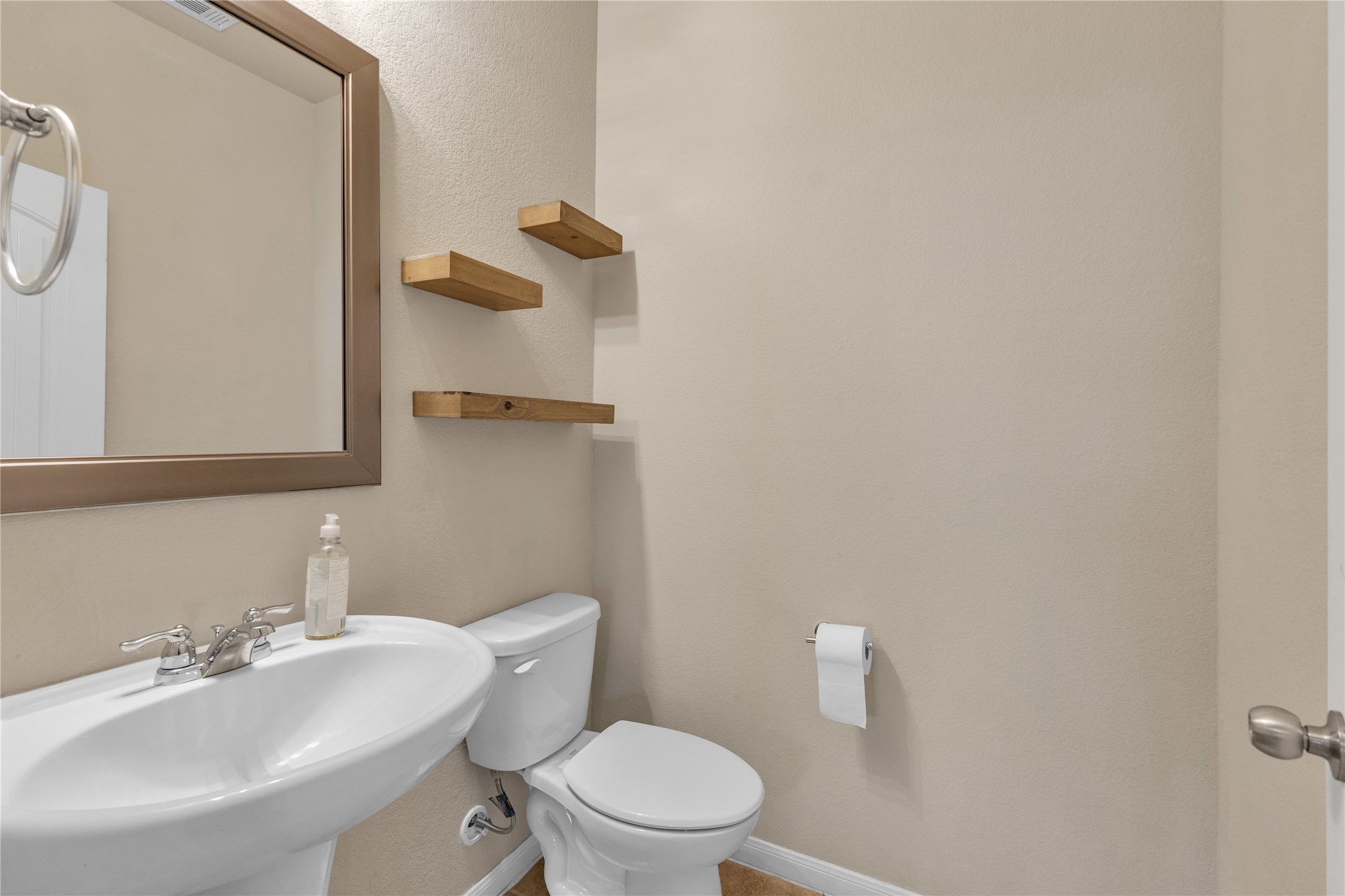 2880 Donnell Drive, Unit 2003 Round Rock, TX 78664 - Photo 16 of 31 Pedestal sink with chrome-finish faucet, framed mirror, and wood-finish floating shelves against neutral-toned walls