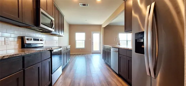 a kitchen with stainless steel appliances granite countertop a refrigerator a sink dishwasher a stove and white countertops with wooden floor