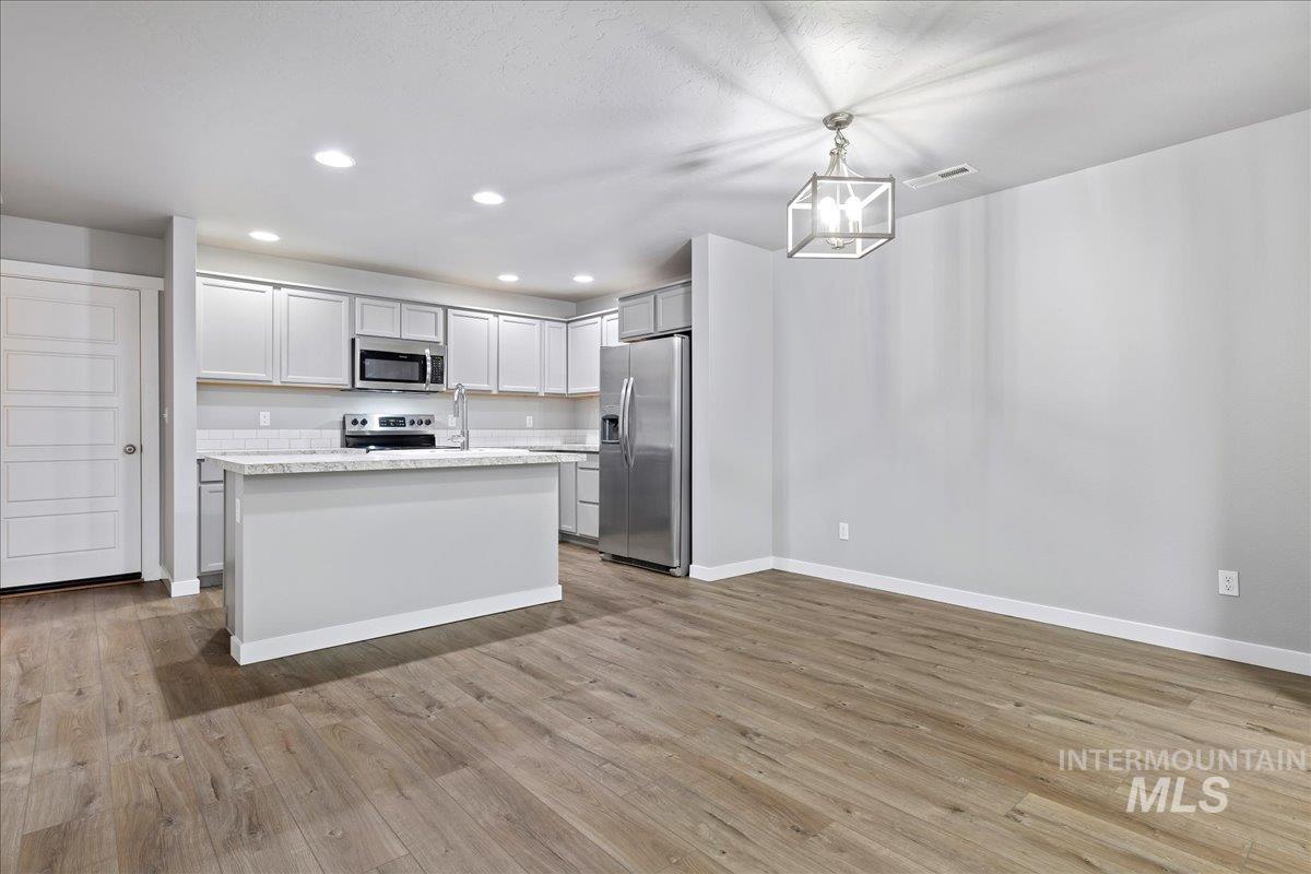 2513 East Goldstone Street Meridian, ID 83642 - Photo 24 of 27 Kitchen with stainless steel appliances, a kitchen island, light wood-type flooring, a chandelier, and open floor plan