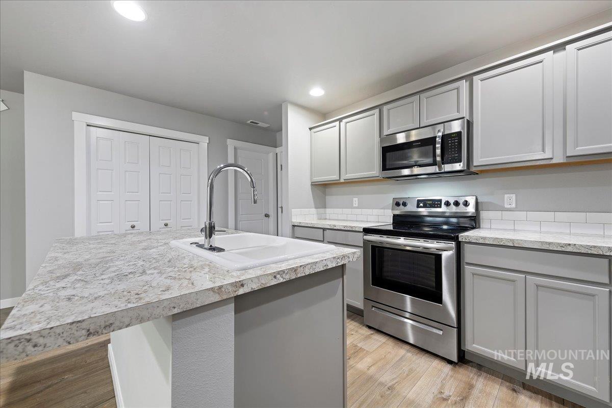 2513 East Goldstone Street Meridian, ID 83642 - Photo 9 of 27 Kitchen featuring gray cabinets, stainless steel appliances, light countertops, a kitchen island with sink, and light wood-type flooring