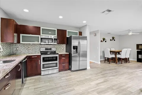 a kitchen with stainless steel appliances granite countertop a stove a refrigerator a sink a dining table and chairs with wooden floor