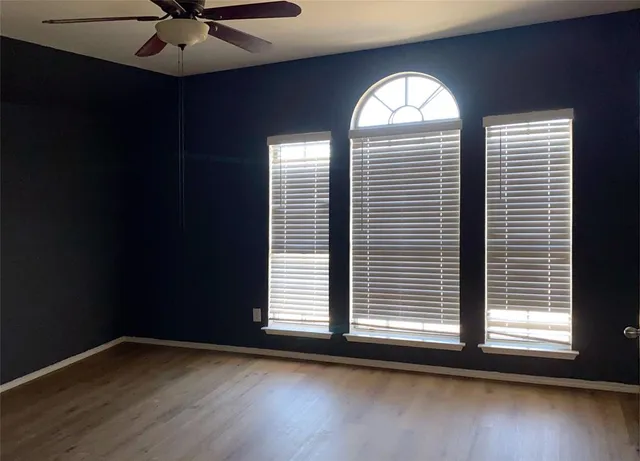 an empty room with wooden floor fan and windows