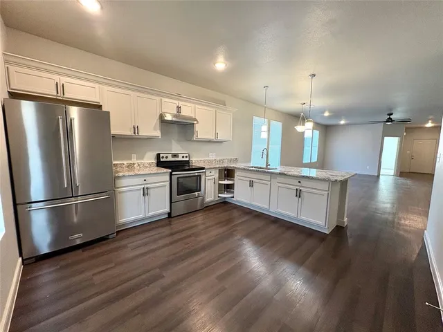 a large kitchen with stainless steel appliances kitchen island a stove a refrigerator a sink dishwasher a oven with white cabinets and wooden floor