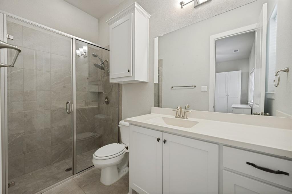 2721 Old Shire Path Road Prosper, TX 75078 - Photo 17 of 39 Spacious bathroom featuring a glass-enclosed shower with tile surround, a single vanity with an integrated sink, white cabinetry, and a large wall mirror