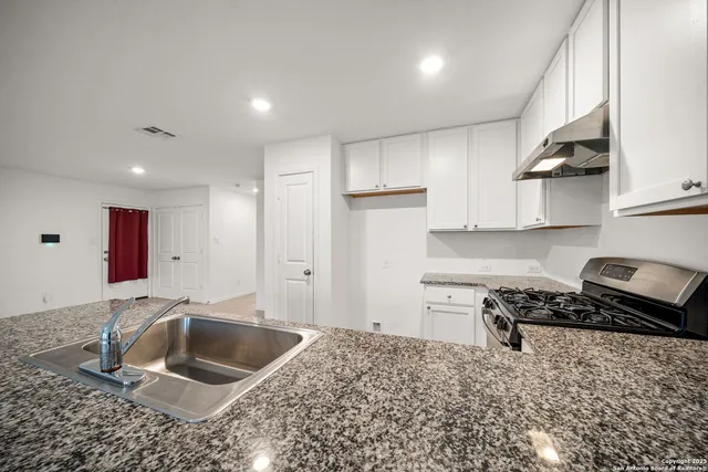 a kitchen with granite countertop a sink a stove and cabinets