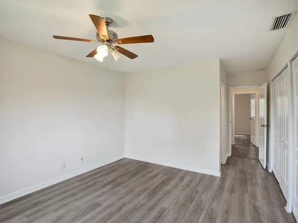 a view of an empty room with wooden floor and a ceiling fan