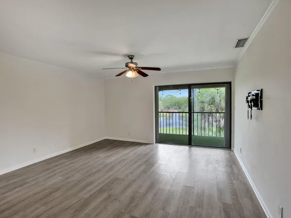 an empty room with wooden floor fan and windows