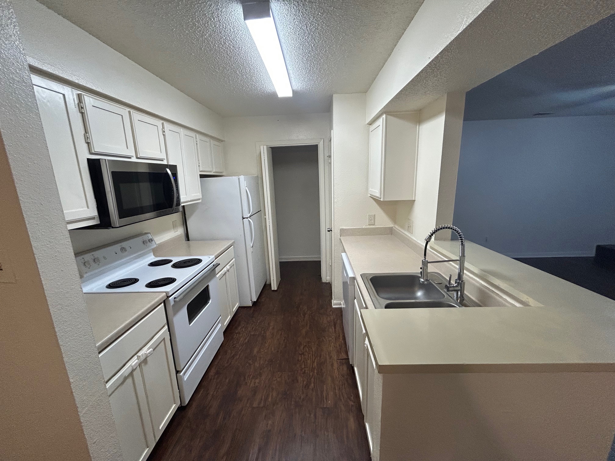 8812 Schick Road, Unit C Austin, TX 78729 - Photo 5 of 12 Kitchen featuring white appliances, dark wood-type flooring, white cabinets, light countertops, and a textured ceiling