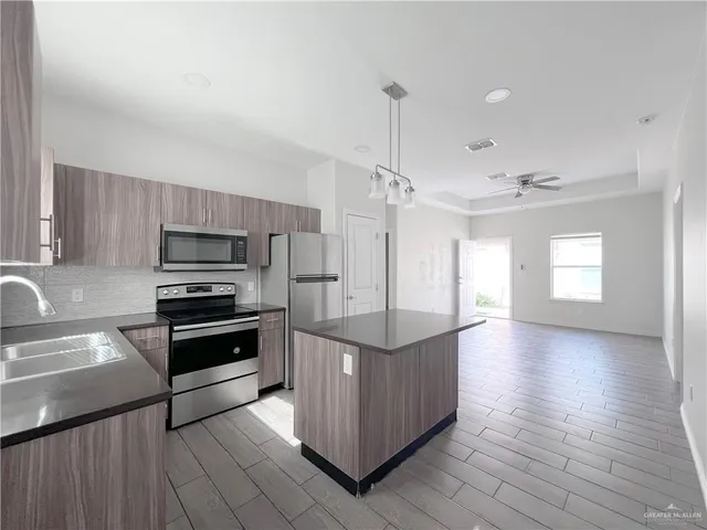 a kitchen with stainless steel appliances kitchen island granite countertop a stove a refrigerator and a sink with wooden floor