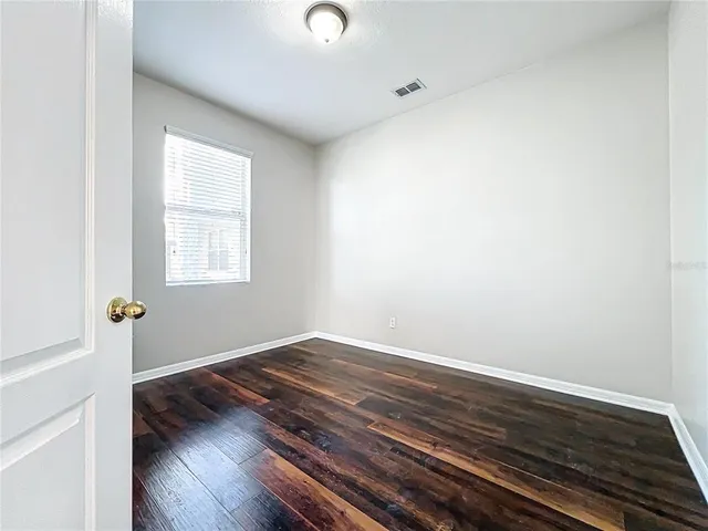 an empty room with wooden floor cabinet and windows
