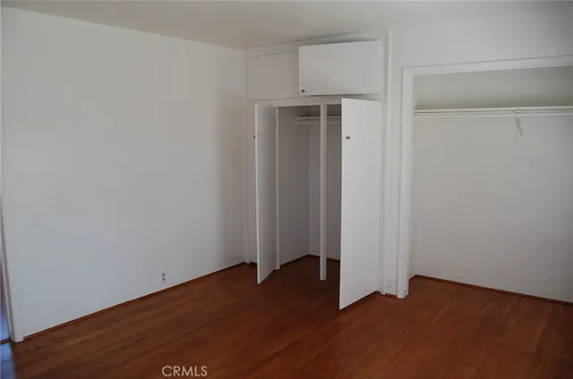 an empty room with wooden floor closet and windows