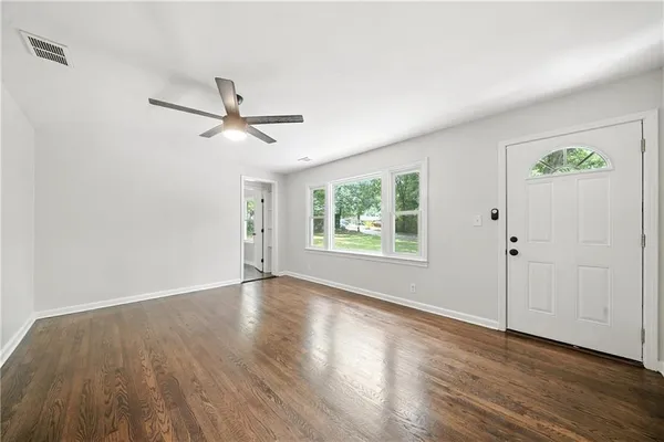 an empty room with wooden floor chandelier fan and windows
