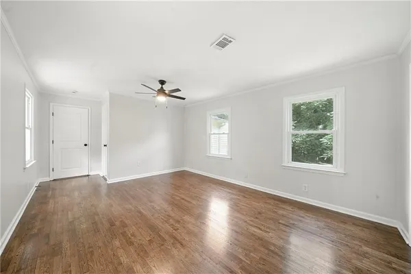 an empty room with wooden floor ceiling fan and windows