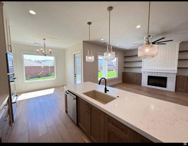 2788 East Rill Drive Washington, UT 84780 - Photo 7 of 41 Open concept living space featuring a central kitchen island with a built-in sink, modern pendant lighting, wood-finish flooring, a contemporary fireplace, and integrated shelving