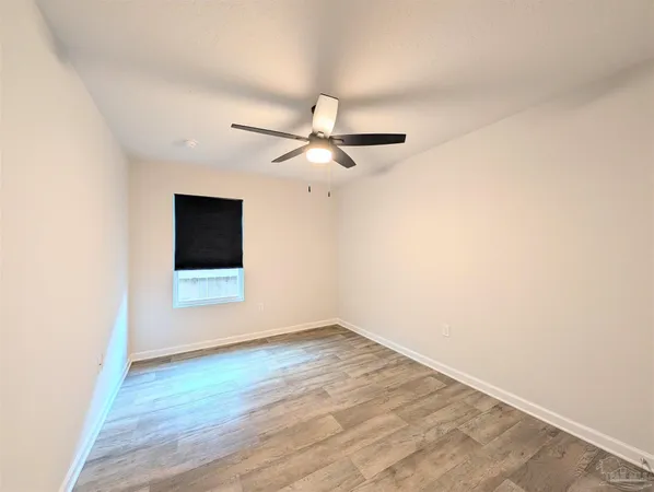 a view of an empty room with wooden floor and a ceiling fan