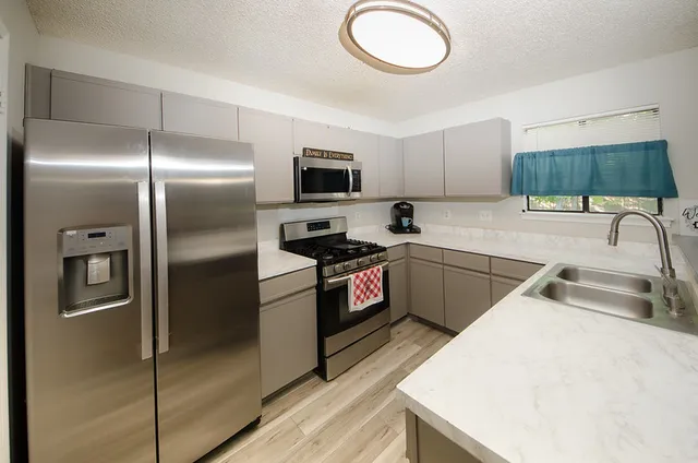 a kitchen with granite countertop a refrigerator a sink a stove top oven and cabinetry