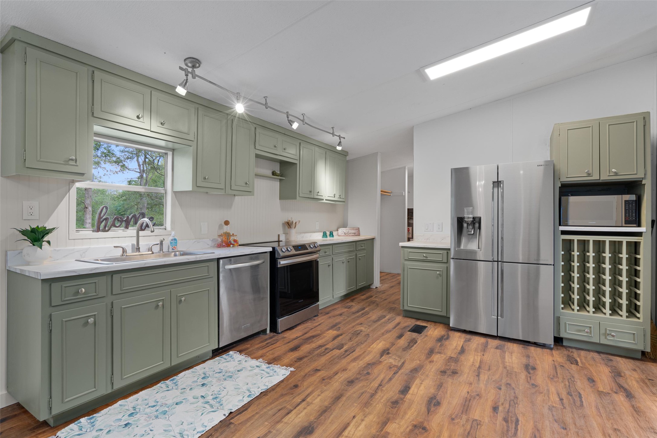 Kitchen with green cabinetry, stainless steel appliances, and dark wood-style floors