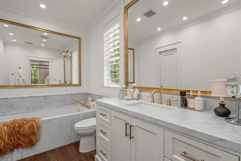 a bathroom with a granite countertop sink mirror vanity bathtub and toilet