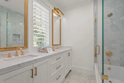 a bathroom with a granite countertop sink two mirror and a shower