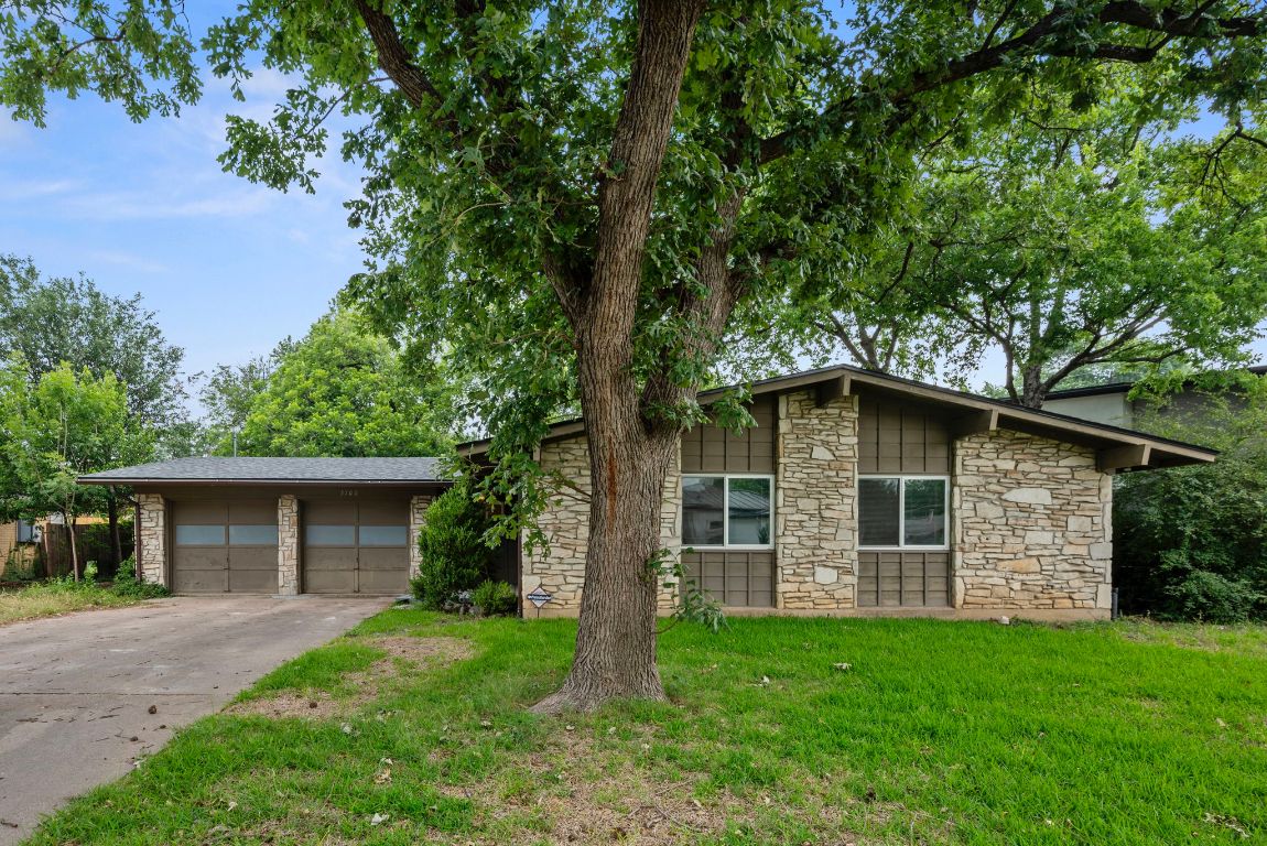 Mid-century modern home featuring stone siding, a front yard, concrete driveway, and a garage
