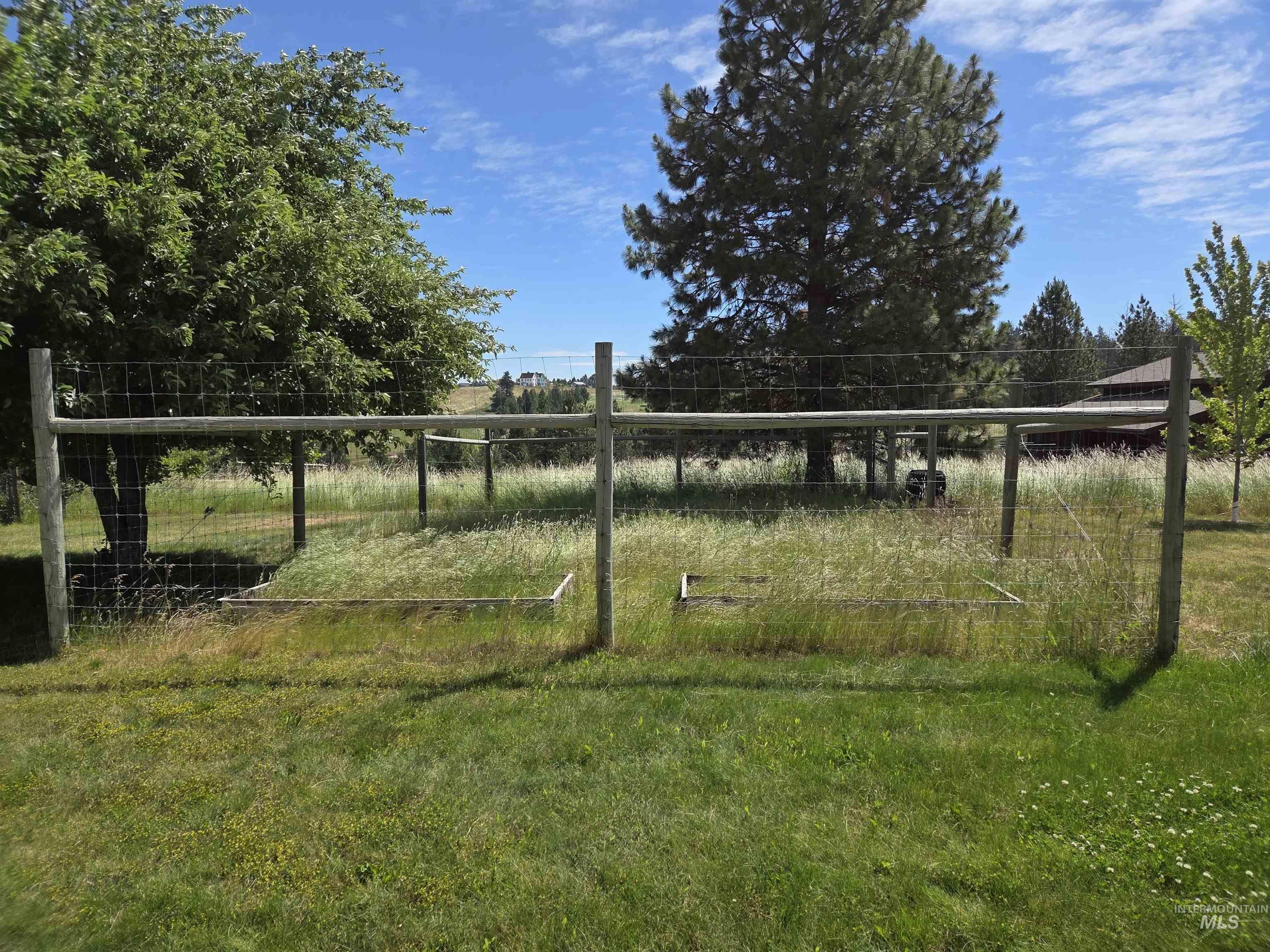 1085 Wallen Road Moscow, ID 83843 - Photo 47 of 50 Expansive fenced area featuring wire mesh and wood post construction, complemented by mature trees and a distant building