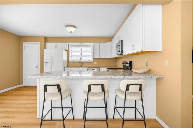 a kitchen with stainless steel appliances granite countertop a stove a sink and white cabinets with wooden floor