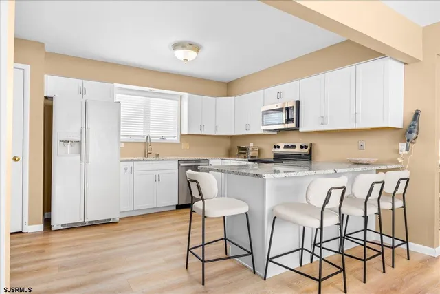 a kitchen with stainless steel appliances granite countertop a stove a sink refrigerator and white cabinets with wooden floor