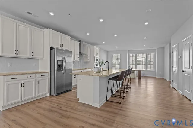 a kitchen with stainless steel appliances granite countertop a refrigerator a stove top oven a sink white cabinets and wooden floor