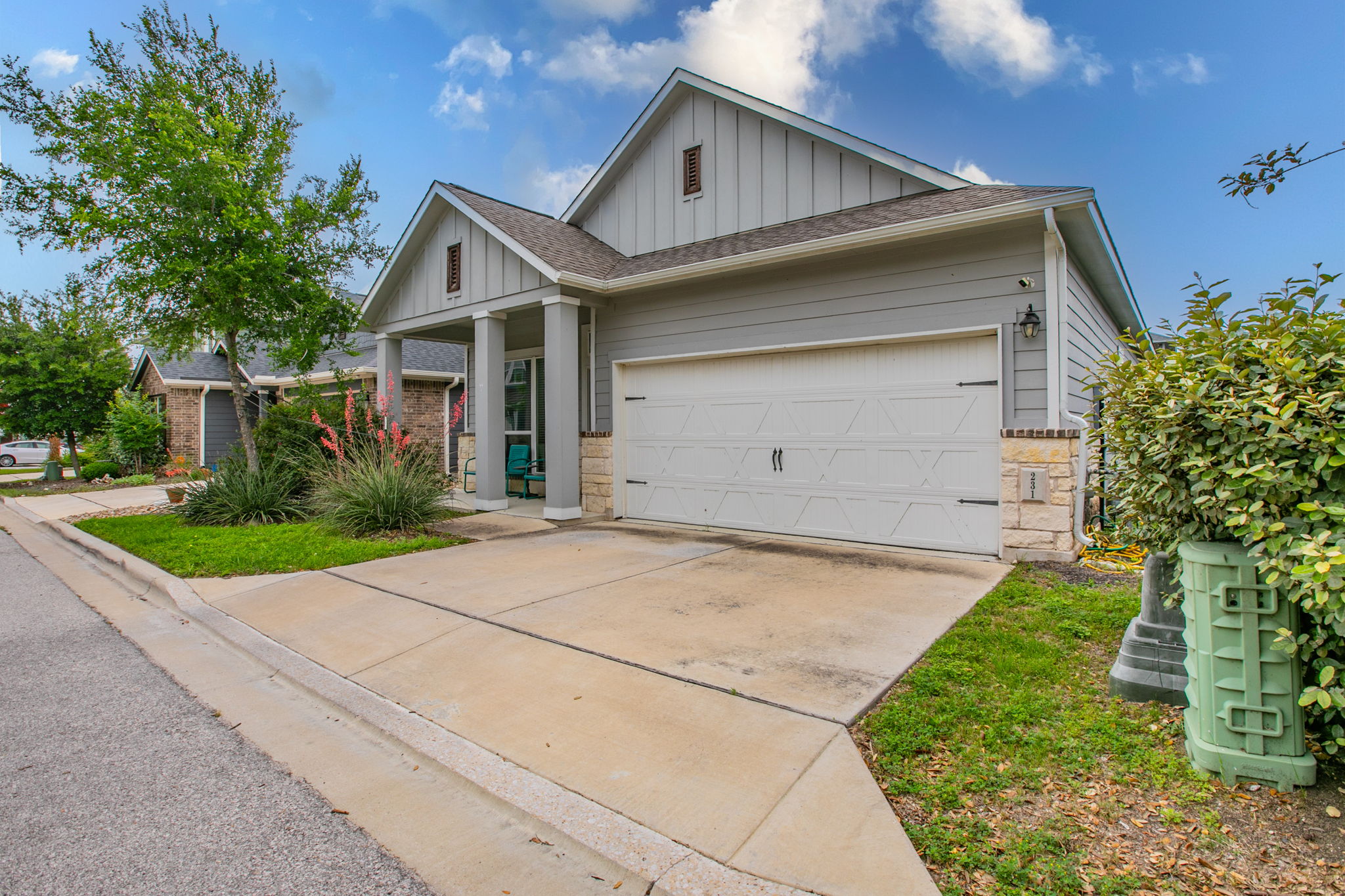 231 Simon Kyle, TX 78640 - Photo 24 of 29 Single-story residence featuring light gray horizontal siding, a prominent front-facing gable with vertical siding accents, and a covered entry porch supported by substantial columns