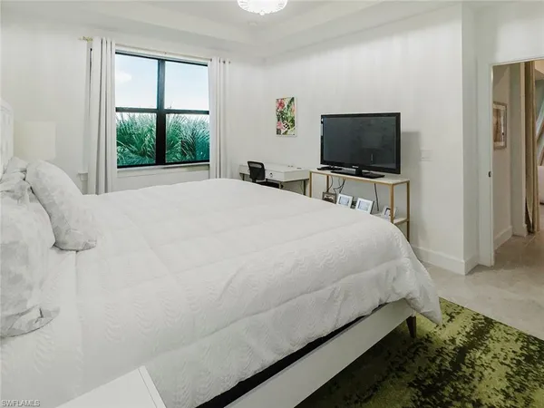 a bedroom with a bed television on desk and a window