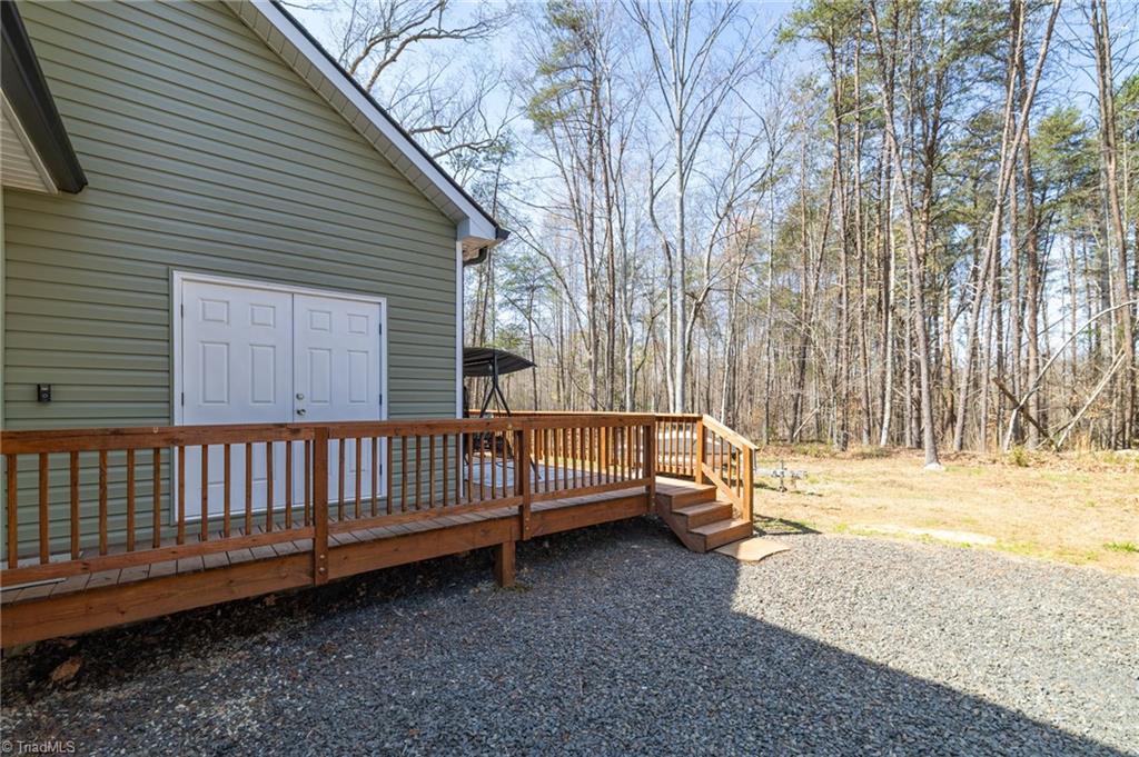 626 Bethany Road Reidsville, NC 27320 - Photo 26 of 42 Back deck at 626 Bethany Road, Reidsville, NC 27320, Rockingham County. Wood deck with railing, double exterior doors, gravel area, and wooded backdrop. Bethany Community.