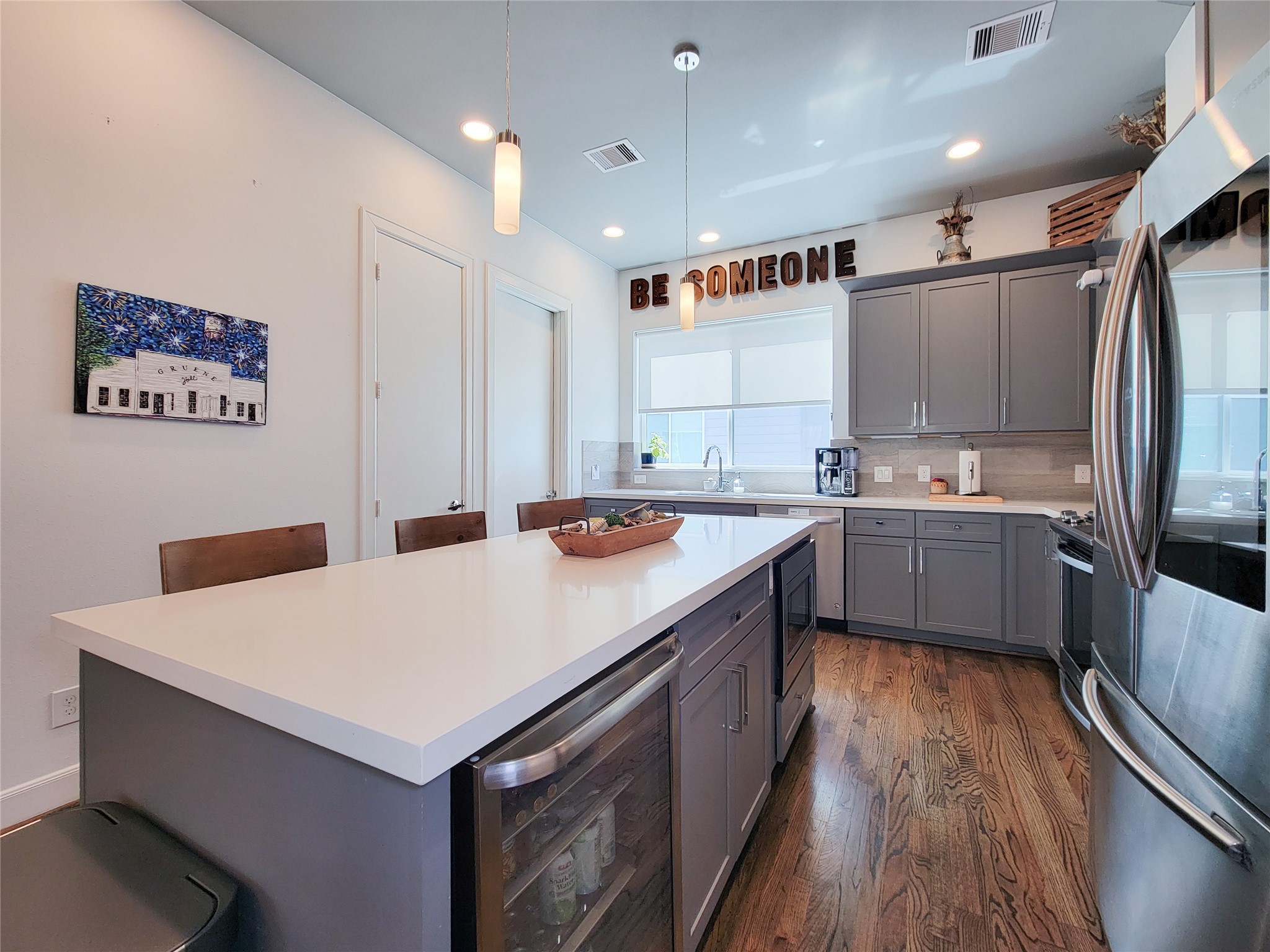 1705 Eado Point Lane Houston, TX 77003 - Photo 27 of 50 This modern kitchen features a spacious island with seating, sleek stainless steel appliances, and ample gray cabinetry. The room is bright and inviting, with hardwood floors and contemporary pendant lighting.