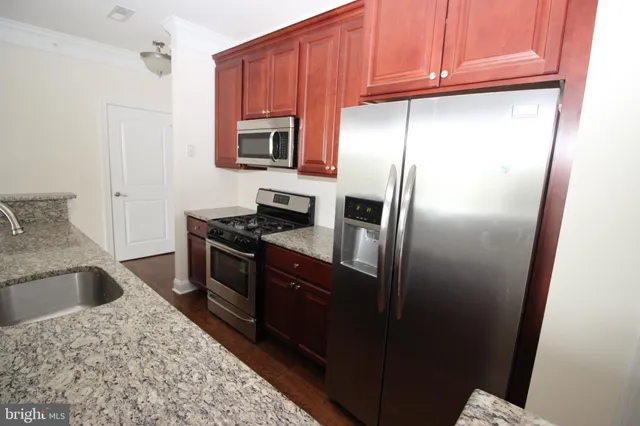 a kitchen with stainless steel appliances granite countertop a refrigerator a stove and a sink with wooden cabinets