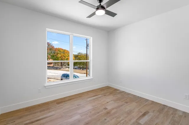 an empty room with wooden floor fan and windows